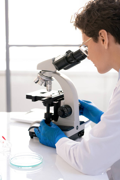 Vista por encima del hombro del investigador de laboratorio concentrado usando microscopio mientras trabaja con muestra médica en laboratorio - Foto, Imagen