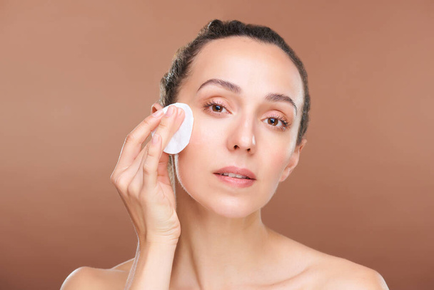 Young woman with natural beauty of her skin applying hydrating toner or micellar water on her face during morning beauty care procedure - Photo, Image