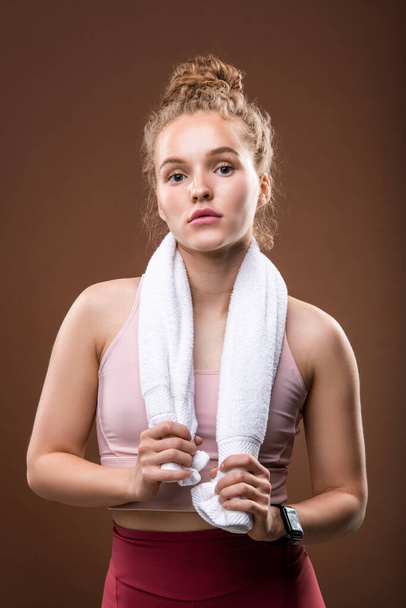 Fit junge Sportlerin mit weichem weißen Handtuch um den Hals, die sich nach dem Sport ausruht, während sie isoliert vor der Kamera steht - Foto, Bild
