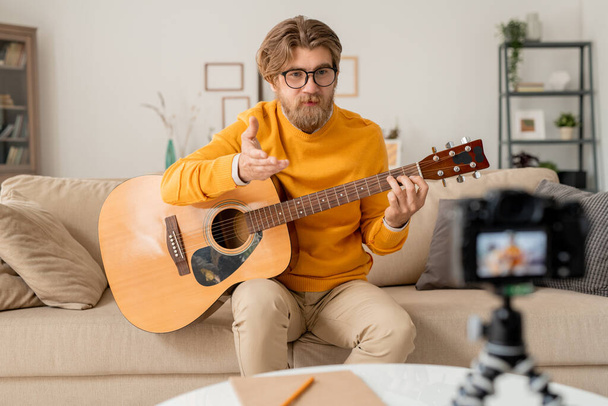 Genç sakallı müzik öğretmeni ev ortamında bir şey anlatıyor ya da çevrimiçi izleyici sorununa cevap veriyor. - Fotoğraf, Görsel