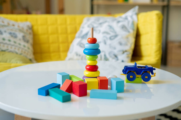 Nagy csoport kis fából készült kockák különböző színekben, műanyag teherautó és halom kék, sárga és piros szakaszok játék pálca az asztalon - Fotó, kép