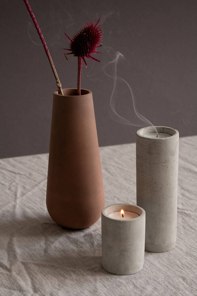 Hygge stijl compositie bestaande uit het branden en uitblazen van kaarsen in wit keramiek glazen en bruine handgemaakte klei vaas met twee gedroogde bloemen - Foto, afbeelding