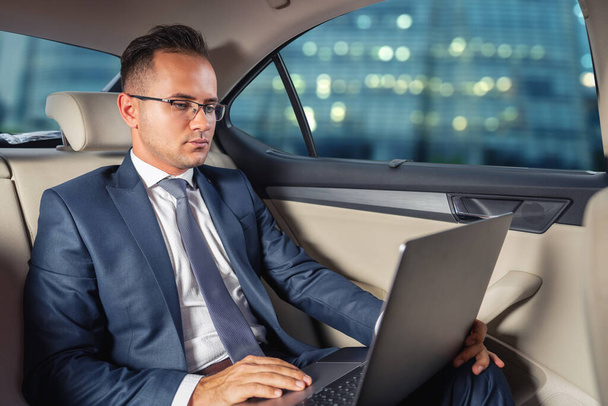 Young businessman using laptop in back seat of car - Foto, immagini