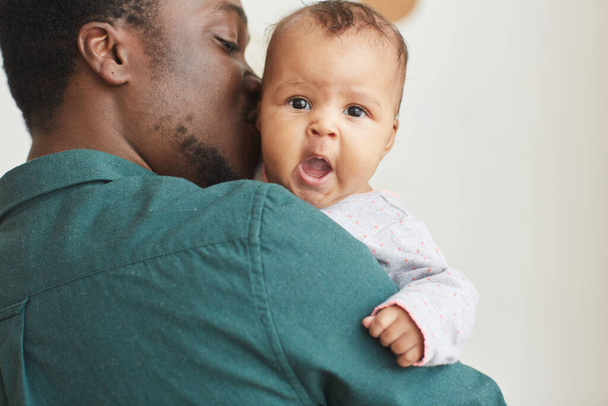 Πλάτη άποψη πορτρέτο του νεαρού Αφροαμερικανού πατέρα κρατώντας γιο με χαριτωμένο μωρό κοιτάζοντας κάμερα πάνω από τους άνδρες ώμο, αντίγραφο χώρο - Φωτογραφία, εικόνα