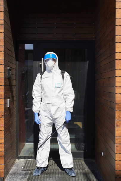 Vertikální portrét pracovníka v ochranném obleku stojícího proti dveřím s dezinfekčním zařízením - Fotografie, Obrázek