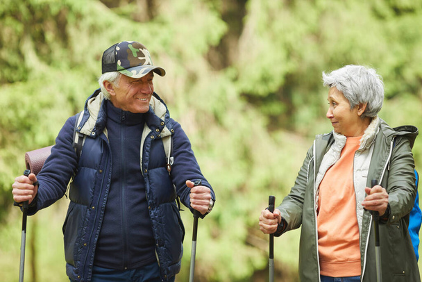 Waist up portrait of cheerful senior couple enjoying Nordic walking with poles during hike in forest - Photo, Image