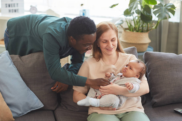 Warm gefärbtes Porträt einer glücklichen interrassischen Familie, die die Zeit zu Hause genießt, mit einem afroamerikanischen Vater, der mit einem pingeligen Baby spielt, Kopierraum - Foto, Bild