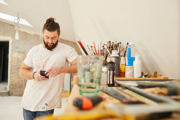 Waist up portrait of contemporary bearded artist using smartphone while standing in spacious art studio, copy space - Zdjęcie, obraz