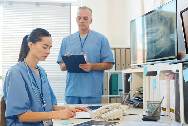 Muotokuva kaksi aikuista lääkäriä yllään sininen univormut kirjallisesti leikepöydälle työskennellessään työpöydän klinikalla sisustus, kopioi tilaa - Valokuva, kuva