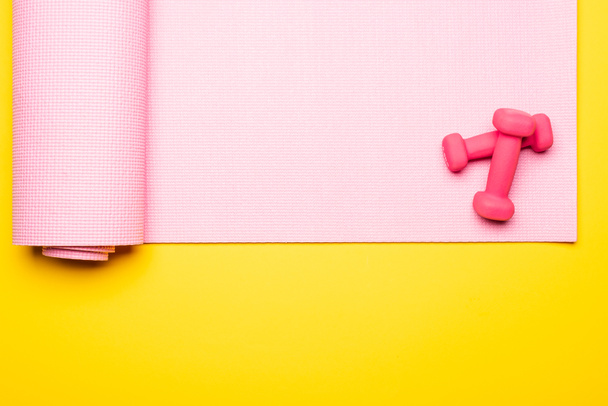 top view of pink fitness mat and dumbbells on yellow background - Fotó, kép