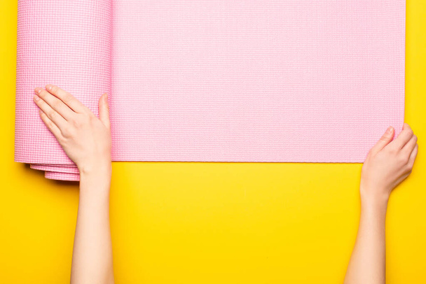 Ausgeschnittene Ansicht einer Frau, die eine rosa Fitnessmatte auf gelbem Hintergrund ausrollt - Foto, Bild