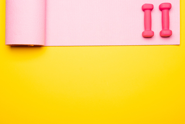 posa piatta con tappeto fitness rosa e manubri su sfondo giallo - Foto, immagini