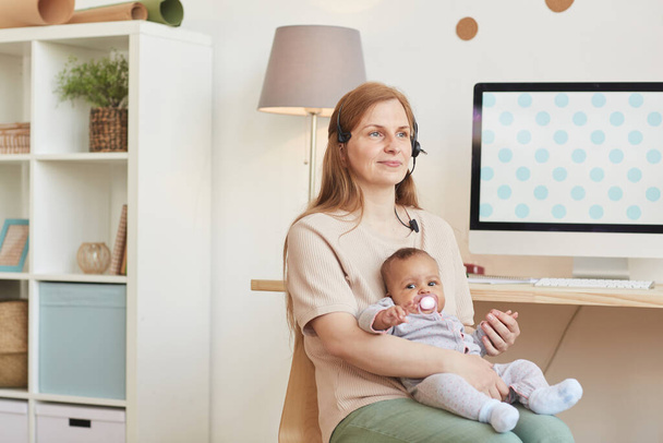 Portret dorosłej pracującej matki trzymającej dziecko i odwracającej wzrok siedząc w biurze domowym, przestrzeń do kopiowania - Zdjęcie, obraz