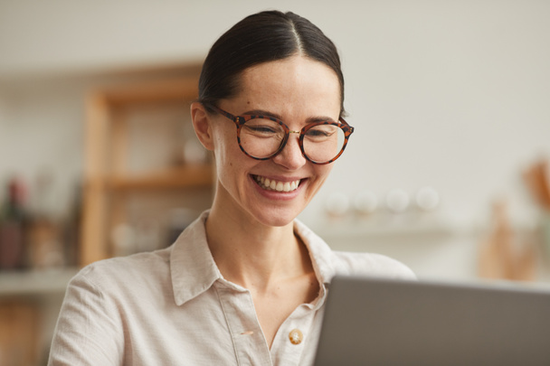 Retrato em tons quentes de jovem empresária usando óculos sorrindo alegremente enquanto olha para a tela do laptop, espaço de cópia - Foto, Imagem