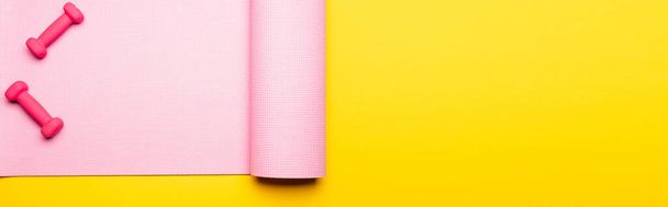 top view of pink fitness mat and dumbbells on yellow background, panoramic shot - Foto, afbeelding