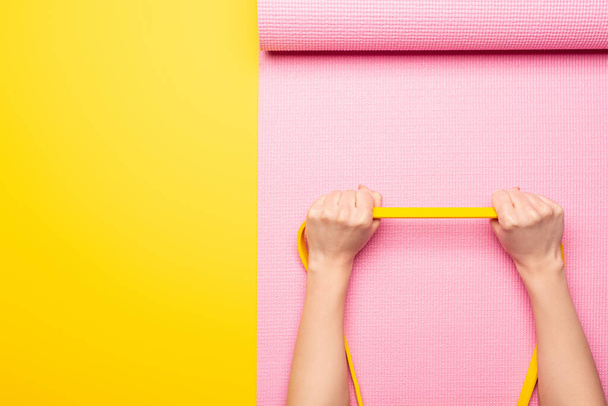 cropped view of woman holding elastic band on pink fitness mat on yellow background - Photo, Image
