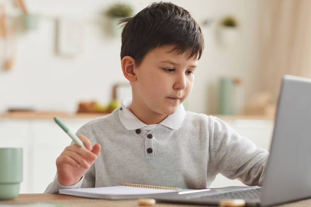 Теплий тоновий портрет милого хлопчика, який навчається вдома, використовуючи ноутбук, що сидить за столом у затишному домашньому інтер'єрі, копіювати простір
 - Фото, зображення
