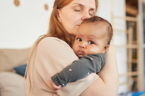 Warm getönte Nahaufnahme Porträt einer liebevollen erwachsenen Mutter, die ihr süßes Baby mit gemischter Rasse umarmt, während sie die Mutterschaft zu Hause genießt, Kopie - Foto, Bild