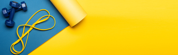 vista dall'alto del tappeto fitness blu con manubri e banda di resistenza su sfondo giallo, scatto panoramico - Foto, immagini