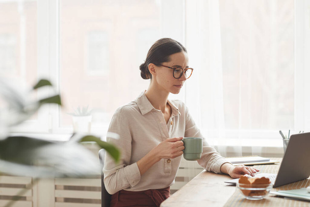 Retrato de vista lateral de mulher de negócios elegante usando óculos ao usar laptop no aconchegante local de trabalho em casa - Foto, Imagem