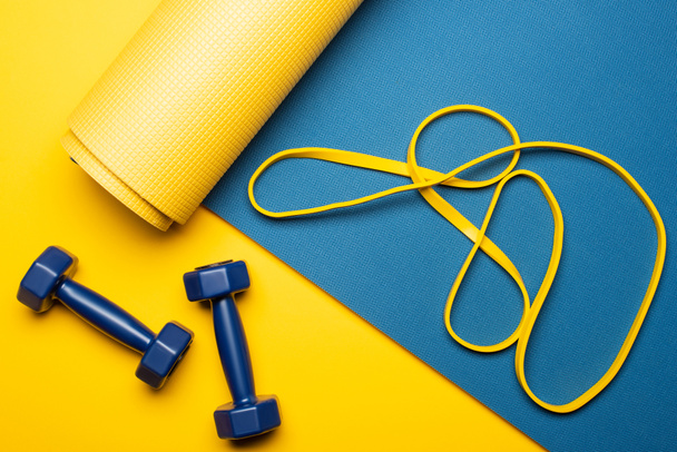 top view of blue fitness mat with dumbbells and resistance band on yellow background - Photo, Image