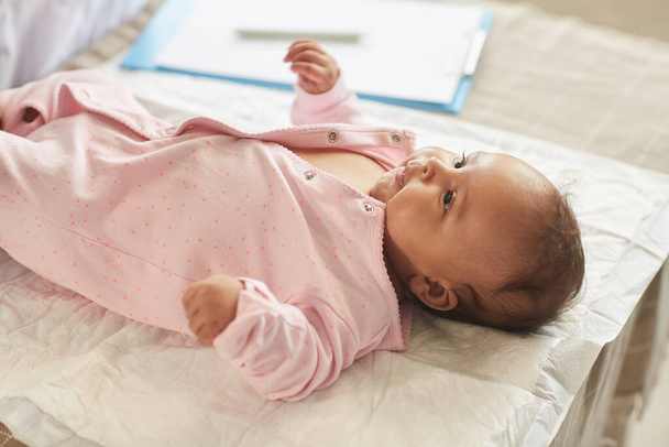 Lämmin ääninen muotokuva söpö vauva tyttö makaa hoitopöydällä lääkärit toimistossa vaaleanpunainen onesie, kopioi tilaa - Valokuva, kuva