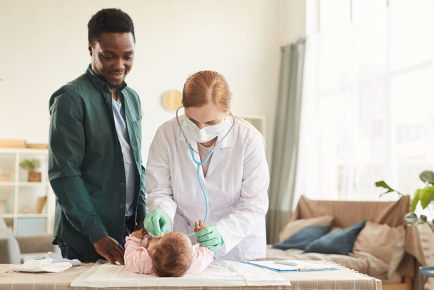 Retrato de la cintura hacia arriba de la doctora examinando al bebé con el padre sonriente de pie junto a ellos, espacio para copiar - Foto, imagen