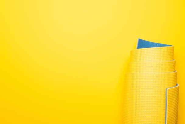 top view of rolled fitness mat on yellow background - Zdjęcie, obraz