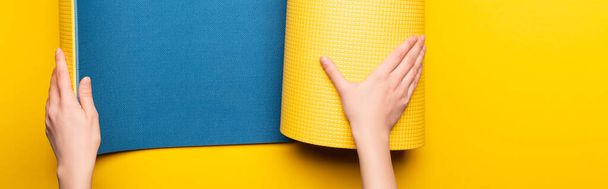 partial view of woman rolling out blue fitness mat on yellow background, panoramic shot - Fotoğraf, Görsel
