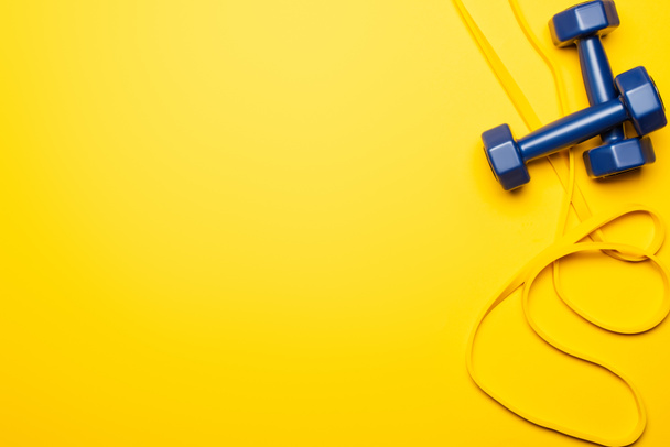 top view of blue dumbbells and resistance band on yellow background - Photo, image