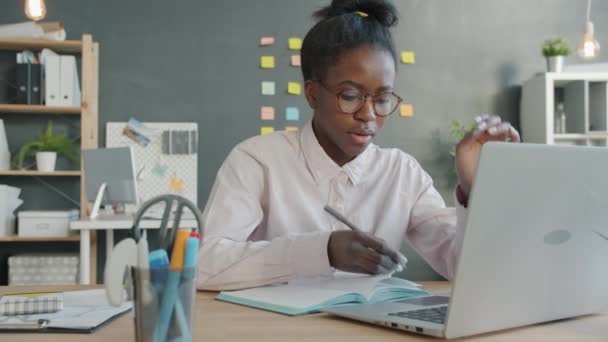 Femme d'affaires afro-américaine utilisant un ordinateur portable prenant des notes dans un cahier à la recherche fatigué et malheureux - Séquence, vidéo