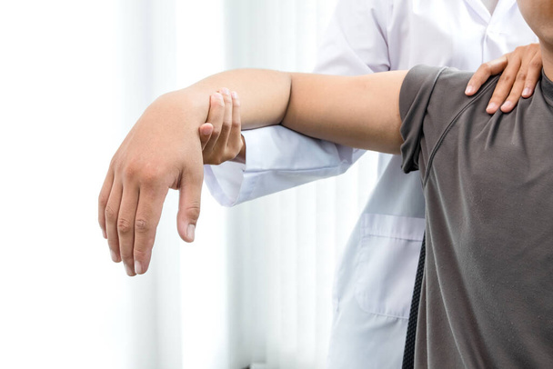 Fisioterapeutas do sexo feminino prestam assistência a pacientes do sexo masculino com lesões no cotovelo para examinar pacientes em centros de reabilitação. Conceito de fisioterapia de reabilitação
. - Foto, Imagem