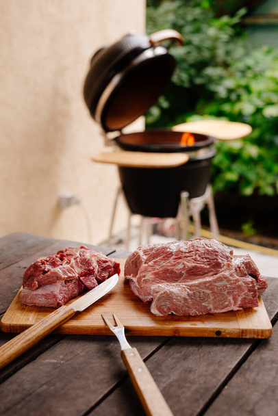 Raw beef. A piece of raw beef cut in half. Raw beef in front of the grill. Grill in the background. - 写真・画像