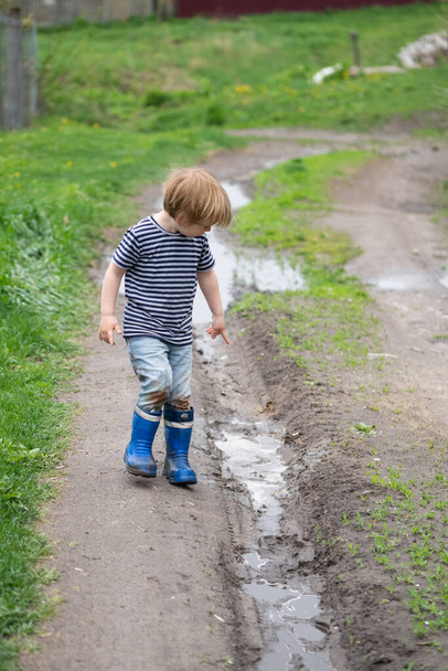 a small boy in rubber boots walks next to a muddy puddle - Foto, afbeelding