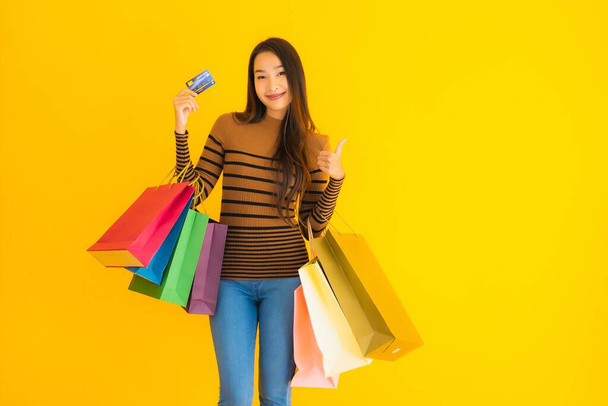 Portret piękna młoda azjatycka kobieta korzystać z karty kredytowej na zakupy z kolorowe zakupy torba na żółtym odizolowanym tle - Zdjęcie, obraz