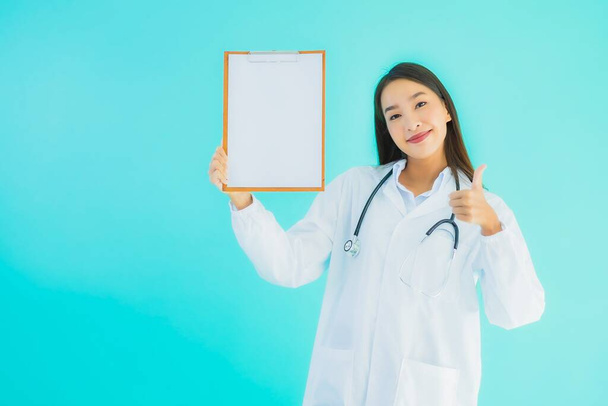 Portrait beautiful young asian doctor woman with empty card billboard banner on blue isolated background - Foto, afbeelding