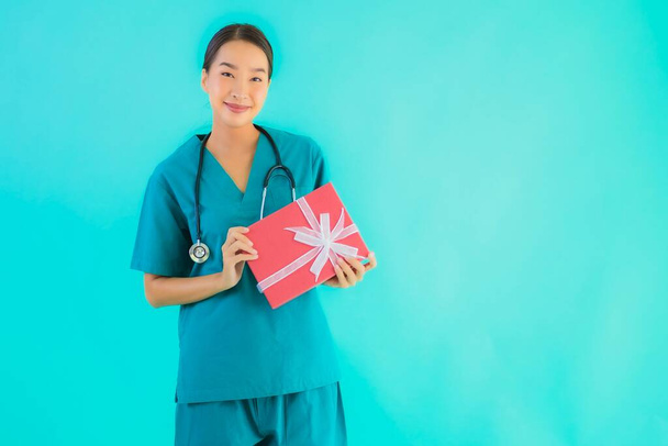 Portret piękny młody Azji lekarz kobieta pokazać czerwony prezent pole na niebieskim odizolowanym tle - Zdjęcie, obraz
