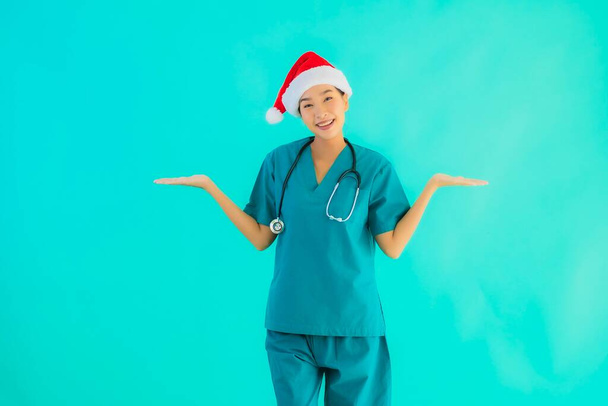 Retrato hermosa joven asiática médico mujer usar navidad sombrero con sonrisa feliz en azul aislado fondo
 - Foto, Imagen