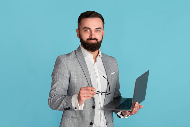 Online work, education or communication. Confident corporate employee with laptop computer on blue background - Valokuva, kuva