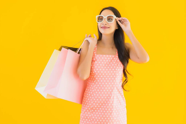 Renkli alışveriş çantalı güzel Asyalı kadın akıllı cep telefonu ve sarı izole edilmiş arka planda kredi kartı. - Fotoğraf, Görsel