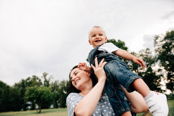 Mutlu, genç bir anne oğlunu elinde tutuyor ve yaz günü çayırda oynarken eğleniyor.  - Fotoğraf, Görsel