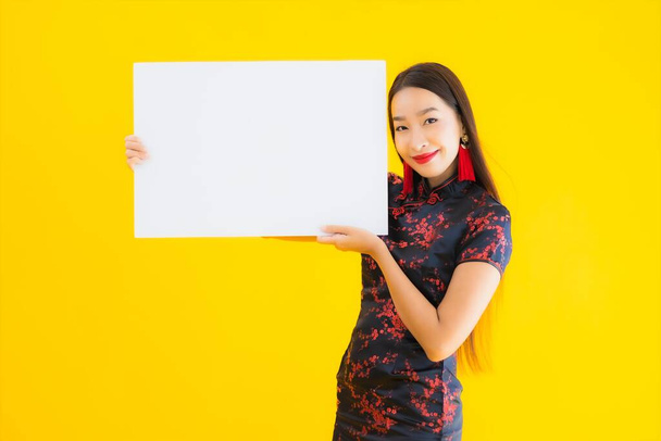 Portrait beautiful young asian woman wear chinese dress show white empty billboard for text in chinese new year concept on yellow isolated background - Zdjęcie, obraz