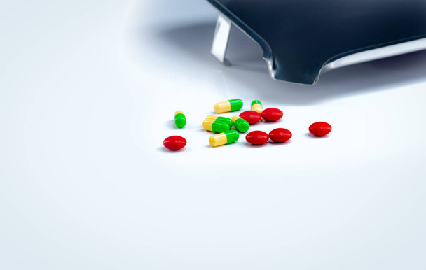 Červené tablety a zelenožluté tobolky s lékem na bílém stole. Farmaceutický průmysl. Vitamíny a doplňky. Farmaceutický koncept. Farmaceutické výrobky. Zdravotní péče a léky. - Fotografie, Obrázek