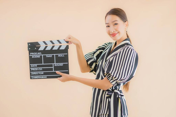 Portret pięknej młodej azjatyckiej kobiety z klaskaczem filmowym na brązowym tle - Zdjęcie, obraz