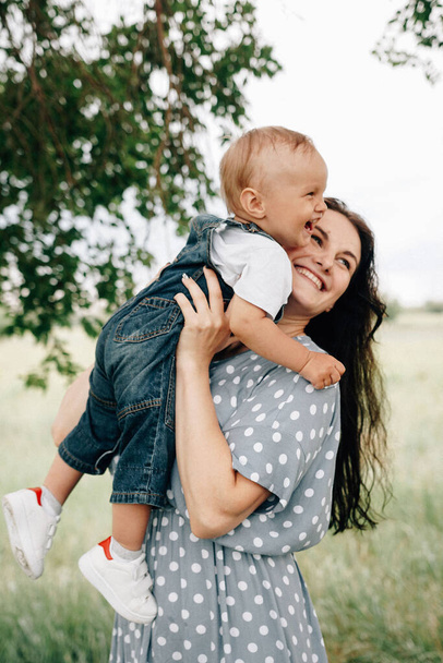 šťastná mladá matka drží syna v rukou a baví se při hraní spolu na louce v letní den  - Fotografie, Obrázek