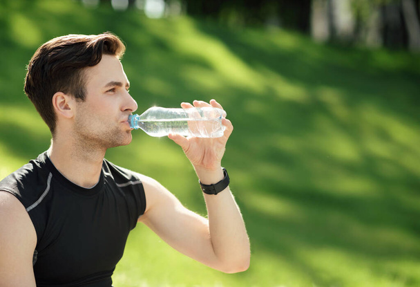 Чоловік п'є воду. Спортсмен зі смарт-годинником тримає пляшку в парку
 - Фото, зображення