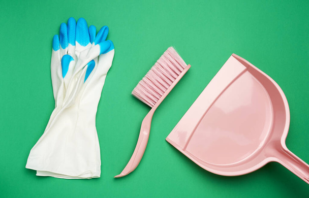 protective white rubber gloves and a pink plastic scoop with a brush on a green background, top view, flat lay - 写真・画像