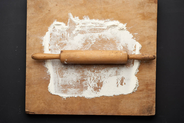 farine de blé blanc éparpillée sur une table en bois et rouleau à pâtisserie en bois sur une table noire, vue du dessus - Photo, image