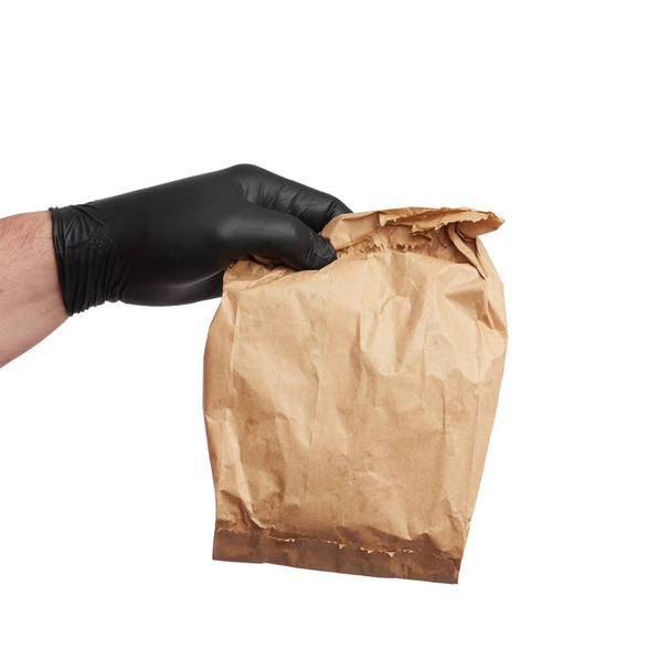 hand in a black latex glove holds a full paper bag of brown craft paper, the concept of remote and contactless food delivery, safe receipt of orders, white background  - Photo, Image