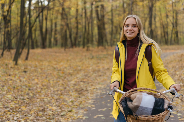 Portrait of beautiful smiling woman riding a bicycle in the park. Autumn concept - Фото, изображение